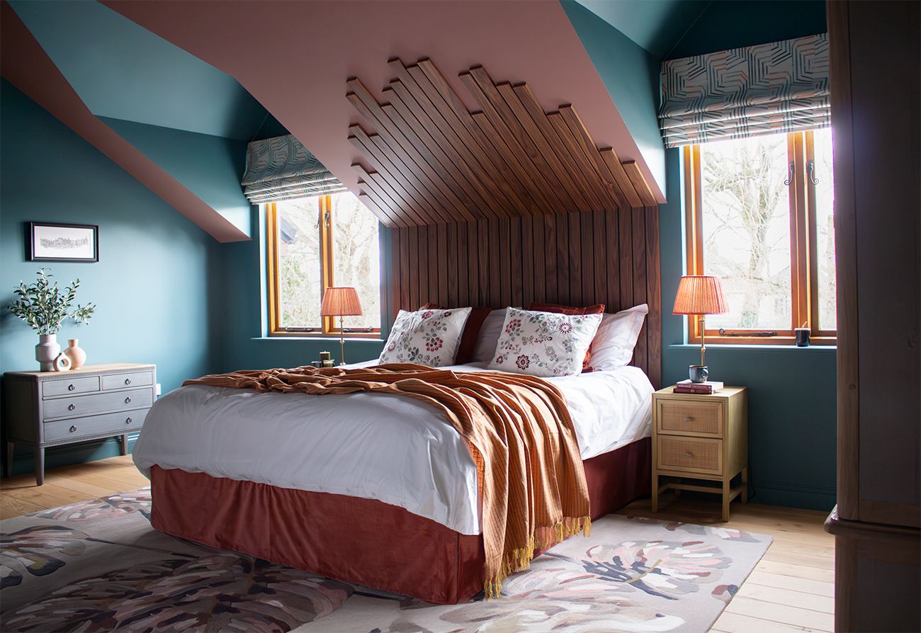 A photo of a main bedroom showing the bed with a terracotta coloured valance,  a bespoke walnut headboard and teal and pink painted walls.