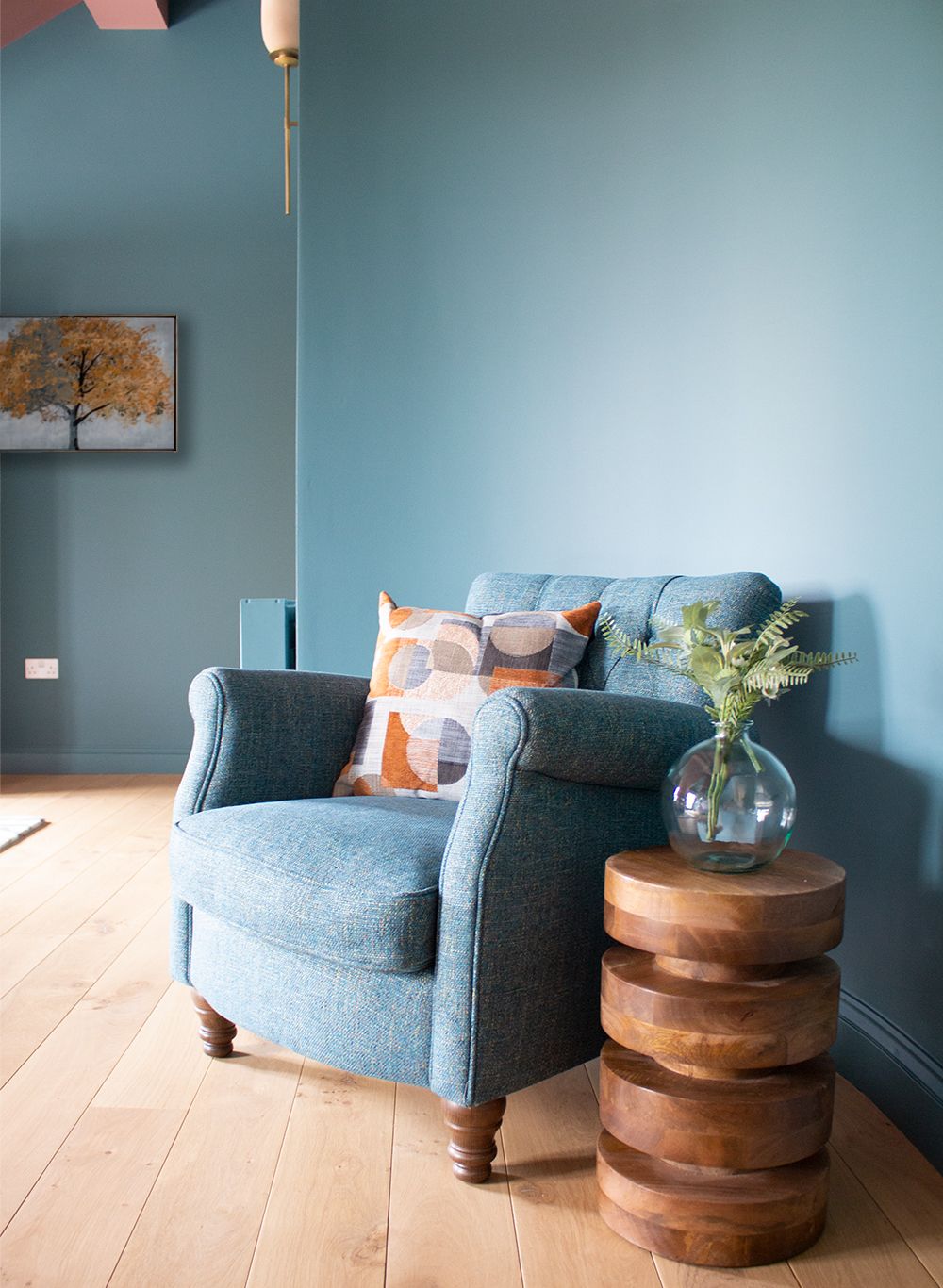 A close up photo of the teal armchair and wooden side table in the main bedroom.