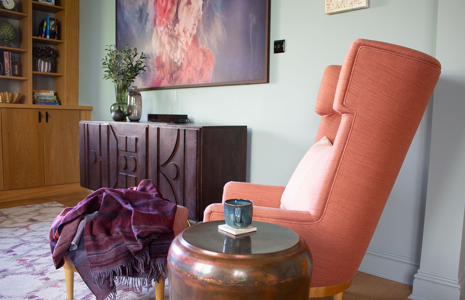 A photo showing a wing back armchair in a soft red, a sideboard and a Samsung Frame TV in a study.