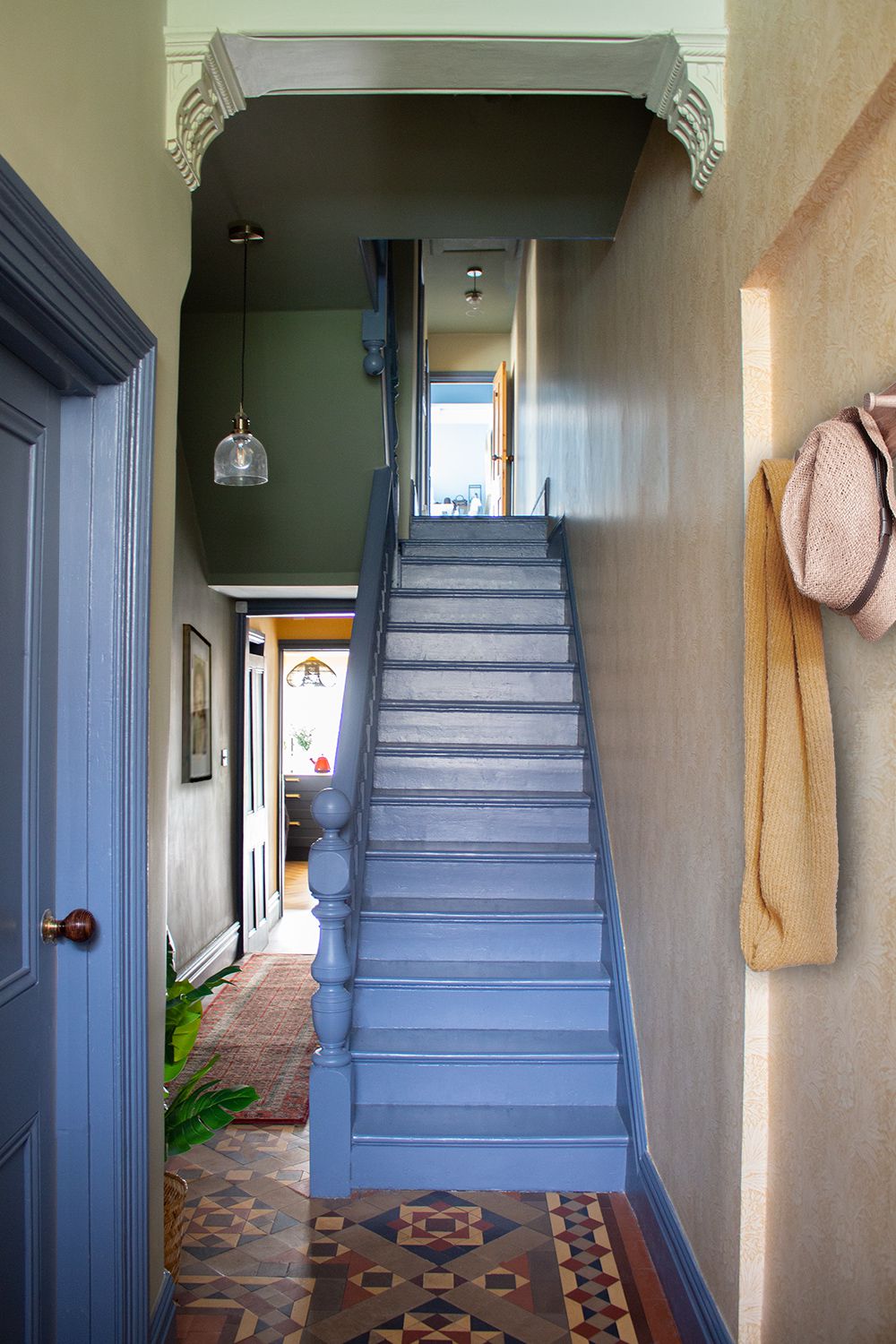 A photo taken at the bottom of the stairs showing the blue painted stairs, yellow wallpaper and ceilings in various shades of green.