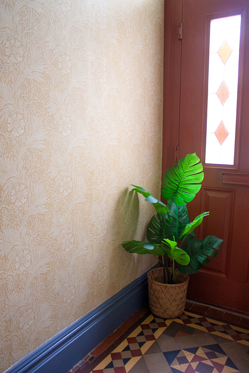 A close up photo of the hallway, showing the red painted front door and a tall plant against the yellow patterned wallpaper.