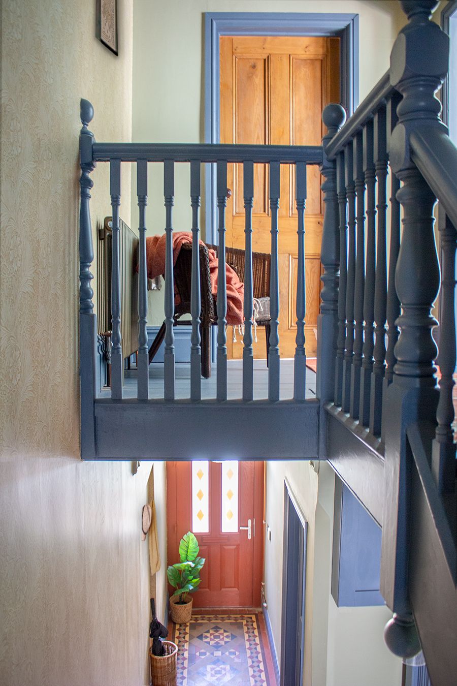 A photo taken from the landing, showing the red front door and the blue bannisters, with a rattan chair on the landing.