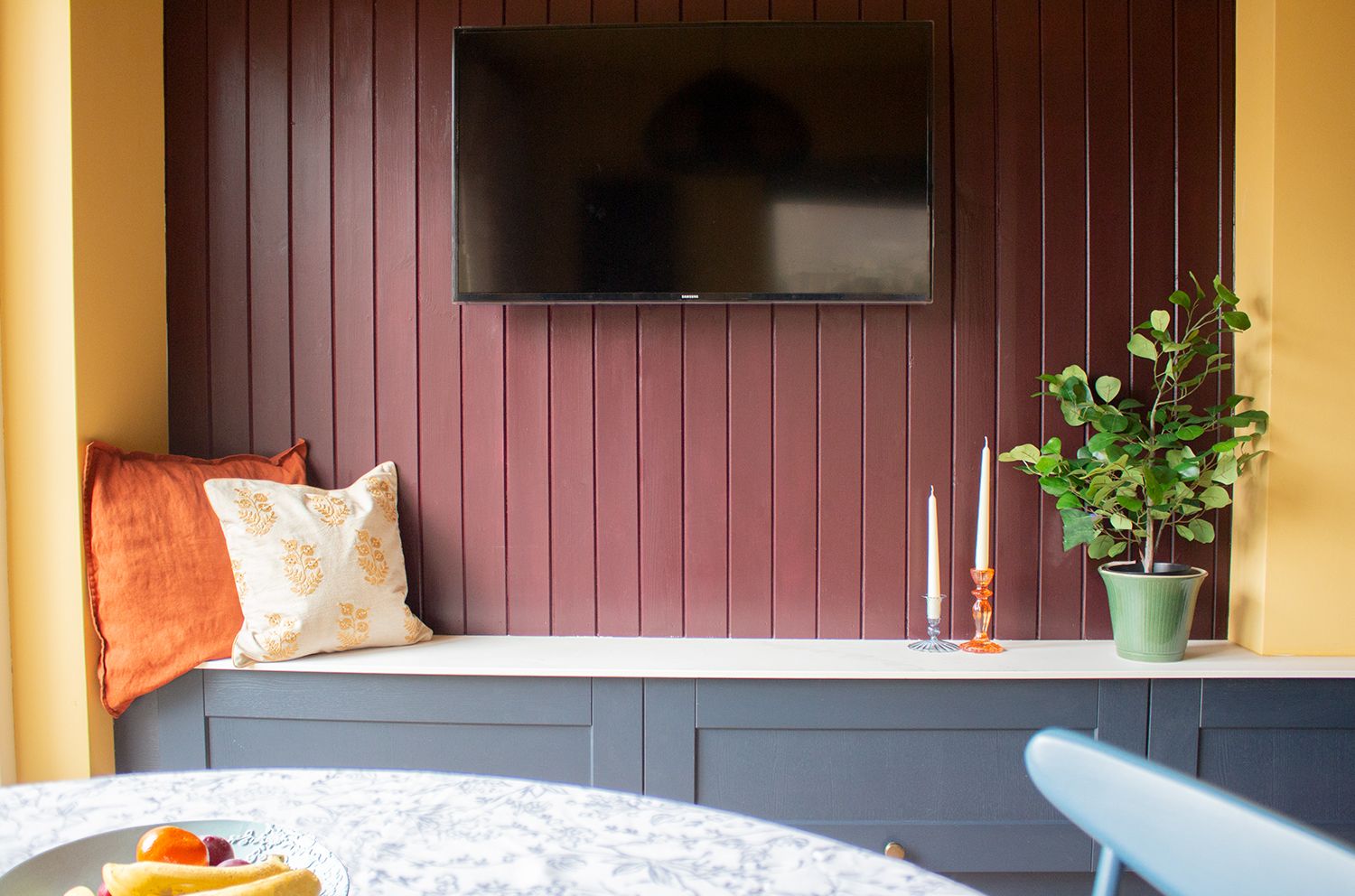 A photo showing the aubergine painted tongue and groove paneling behind the TV, with the bench seating in front.