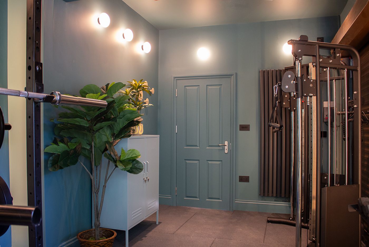 A photo of the home gym, looking towards the door and showing the wall lights and weights equipment.