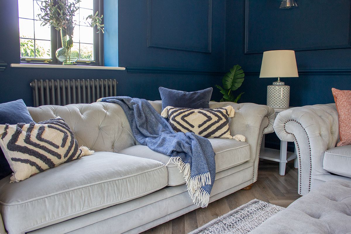 A photo of the corner of the living room, with two comfortable velvet sofas and blue throws and cushions on them.