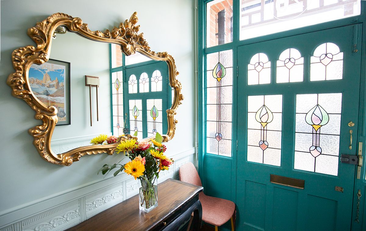 A photo of the teal front door in the hallway with a large gilt mirror on the wall above a console table.