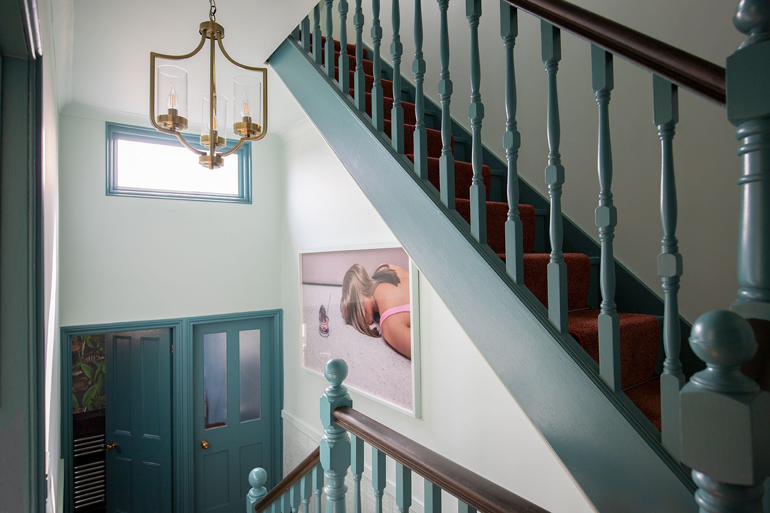 A photo of the first floor landing with teal painted bannisters and brass lighting and door furniture.
