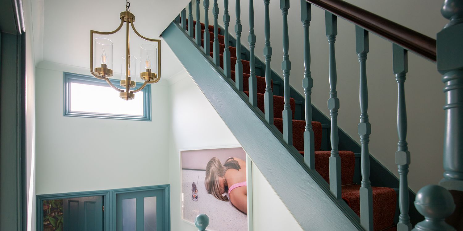 A photo of a landing with the bannisters painted in teal and with an antique brass light fitting.