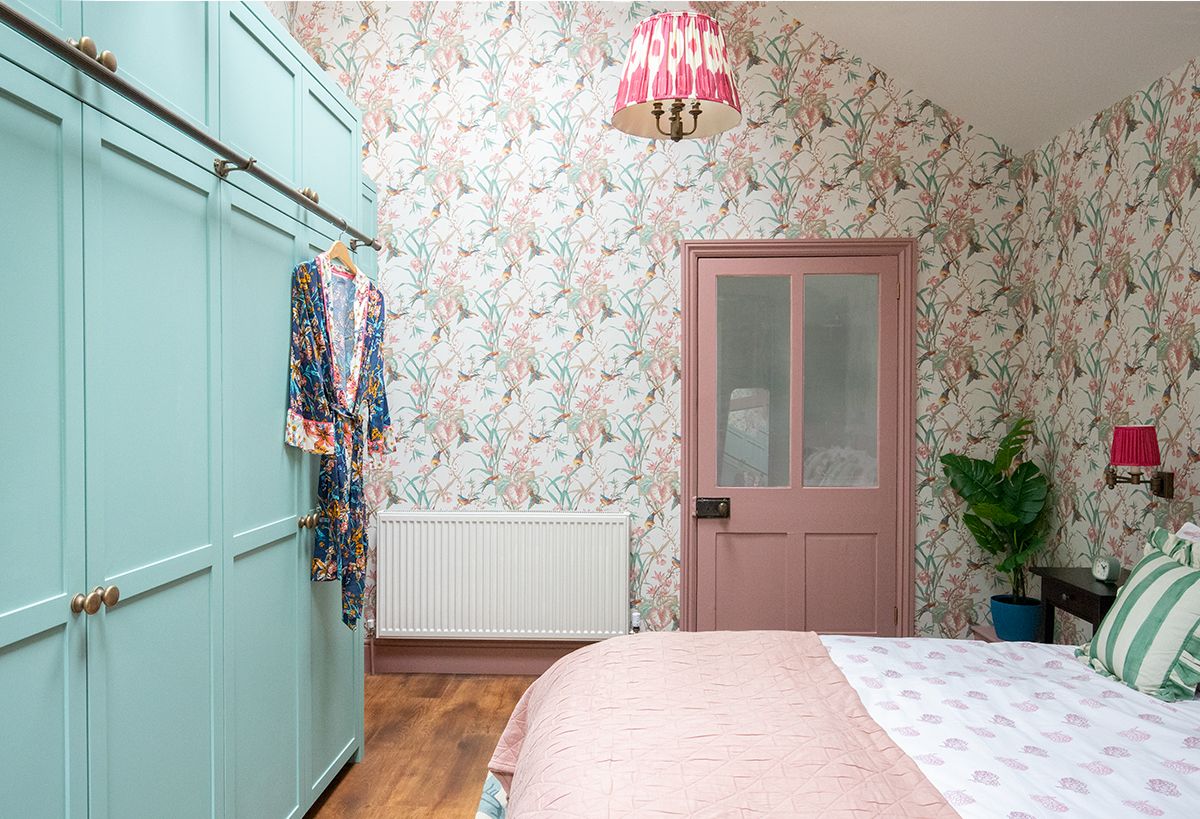 A photo looking towards the pink painted en suite door, with the floral wallpaper all around the room.