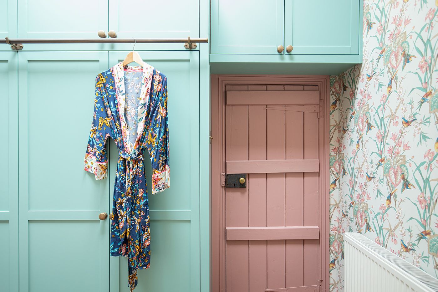 A photo looking at the pink painted original bedroom door, with the green wardrobes surrounding it.