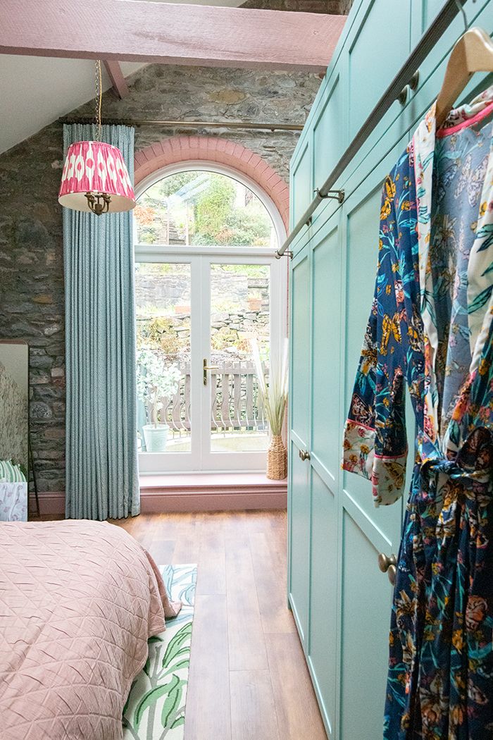 A photo looking along the wardrobe doors towards the single curtain over the French doors. You can see the green, cream and blue rug under the bed.