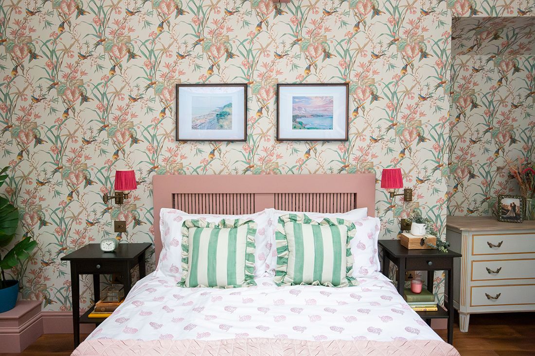 A photo looking straight at the pink bed, with the wallpaper behind and two Welsh landscape prints on the wall above the bed.