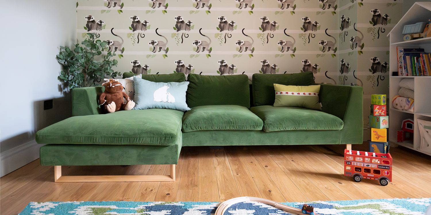 A photo of a playroom with monkey wallpaper and a green velvet corner sofa.