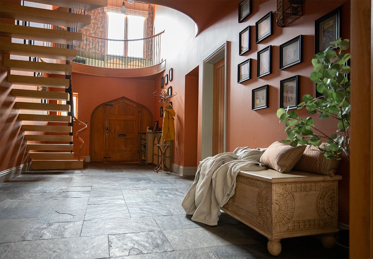 A photo of the hallway looking towards the front door. The walls are painted in an orange red, and the woodwork is a sage green, with built in storage.