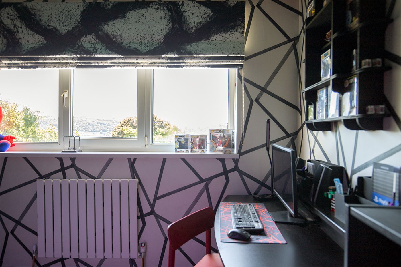 A photo showing the window with a graphic grey, black and white Roman blind, and the white and dark grey lined wallpaper.