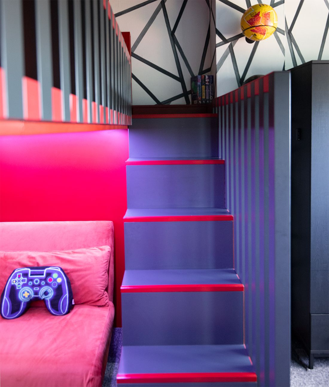 A close up photo of the stairs up to the new cabin bed, which are dark grey with the edges of the steps highlighted in red. You can also see the orange sleepover bed  next to the stairs.