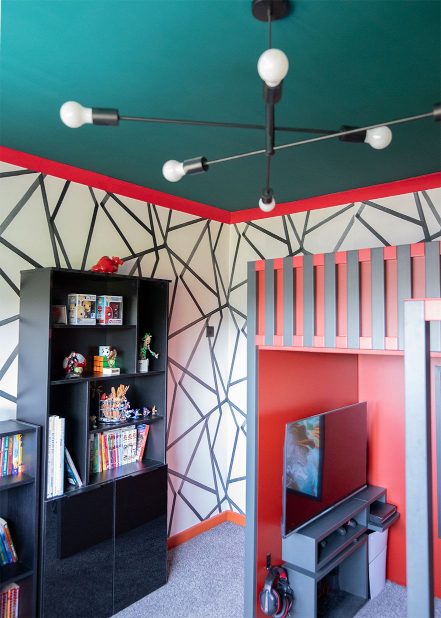 A photo of the end of the bed where there is a large TV mounted with shelving for gaming equipment underneath.