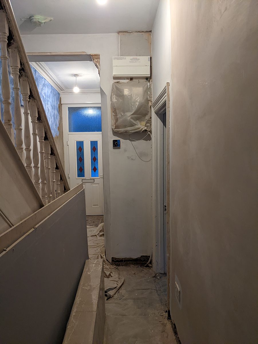 A before photo showing the white painted stairs looking towards the white front door and the new meter cupboard.