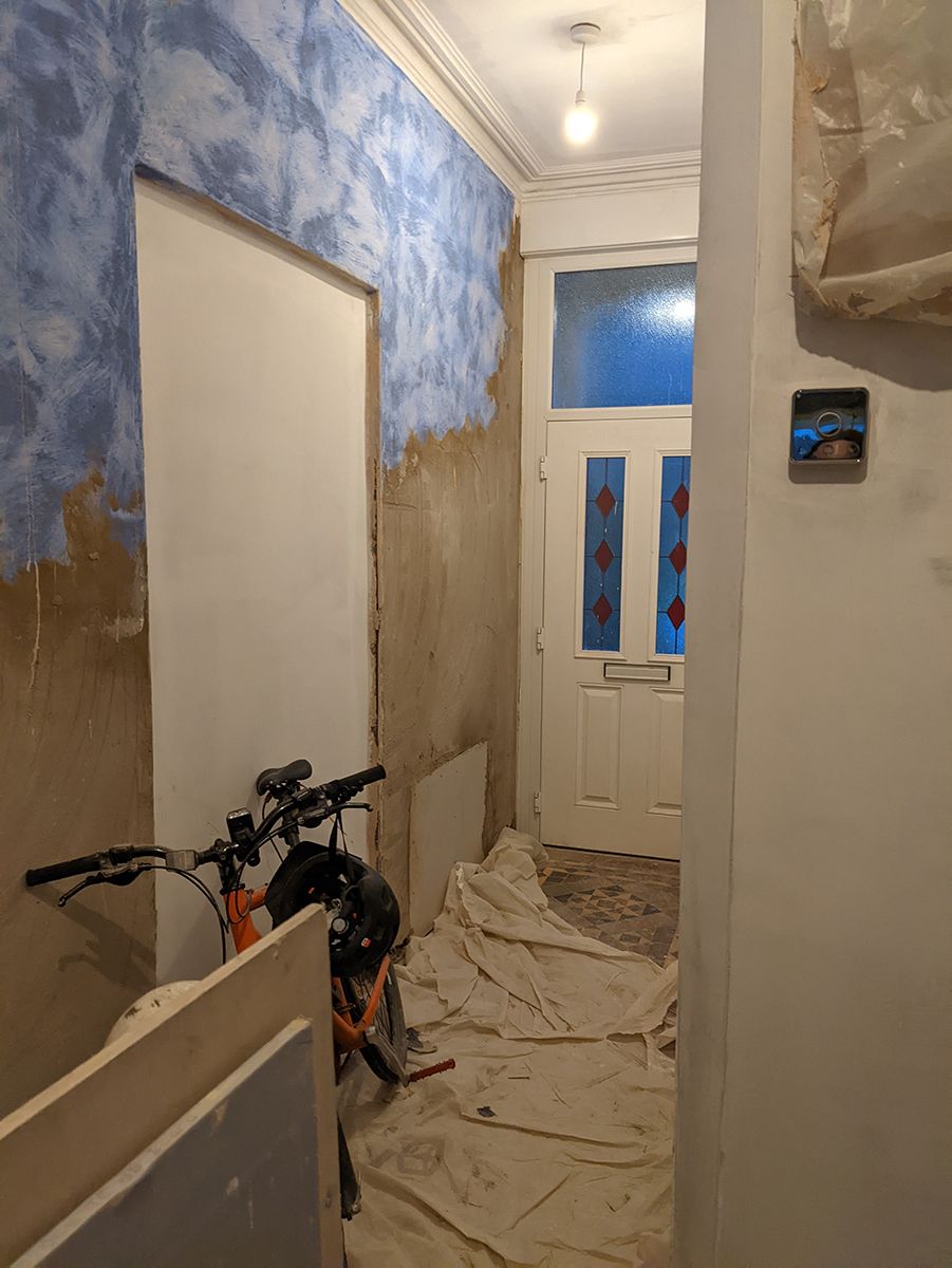 A before photo of the hallway showing the white front door and un plastered walls.