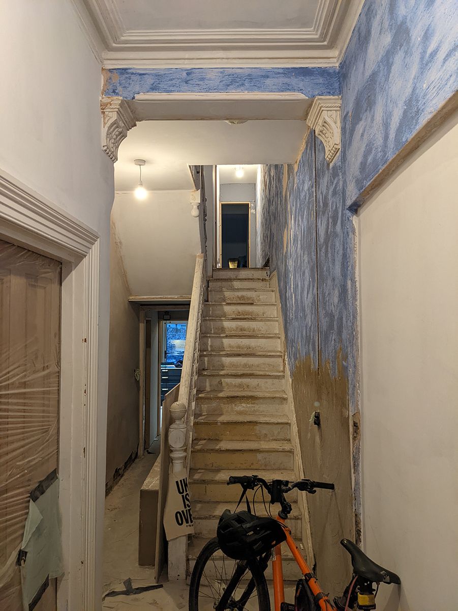 A photo showing the hallway before work started, with un plastered walls and no pint on the stairs.