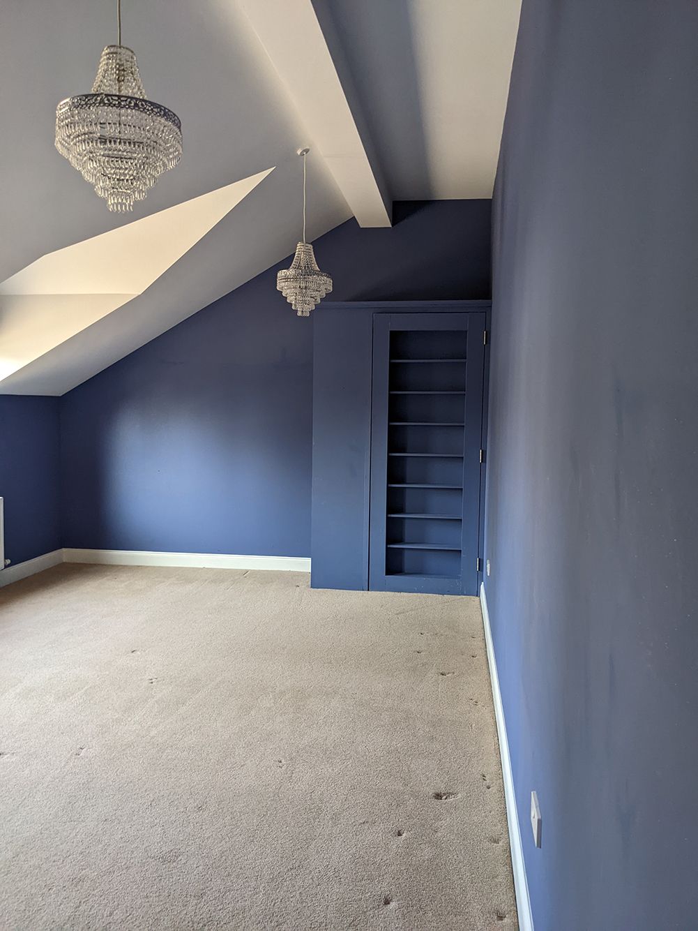 A before photo of the bedroom which had deep purple walls and small chandelier lighting.