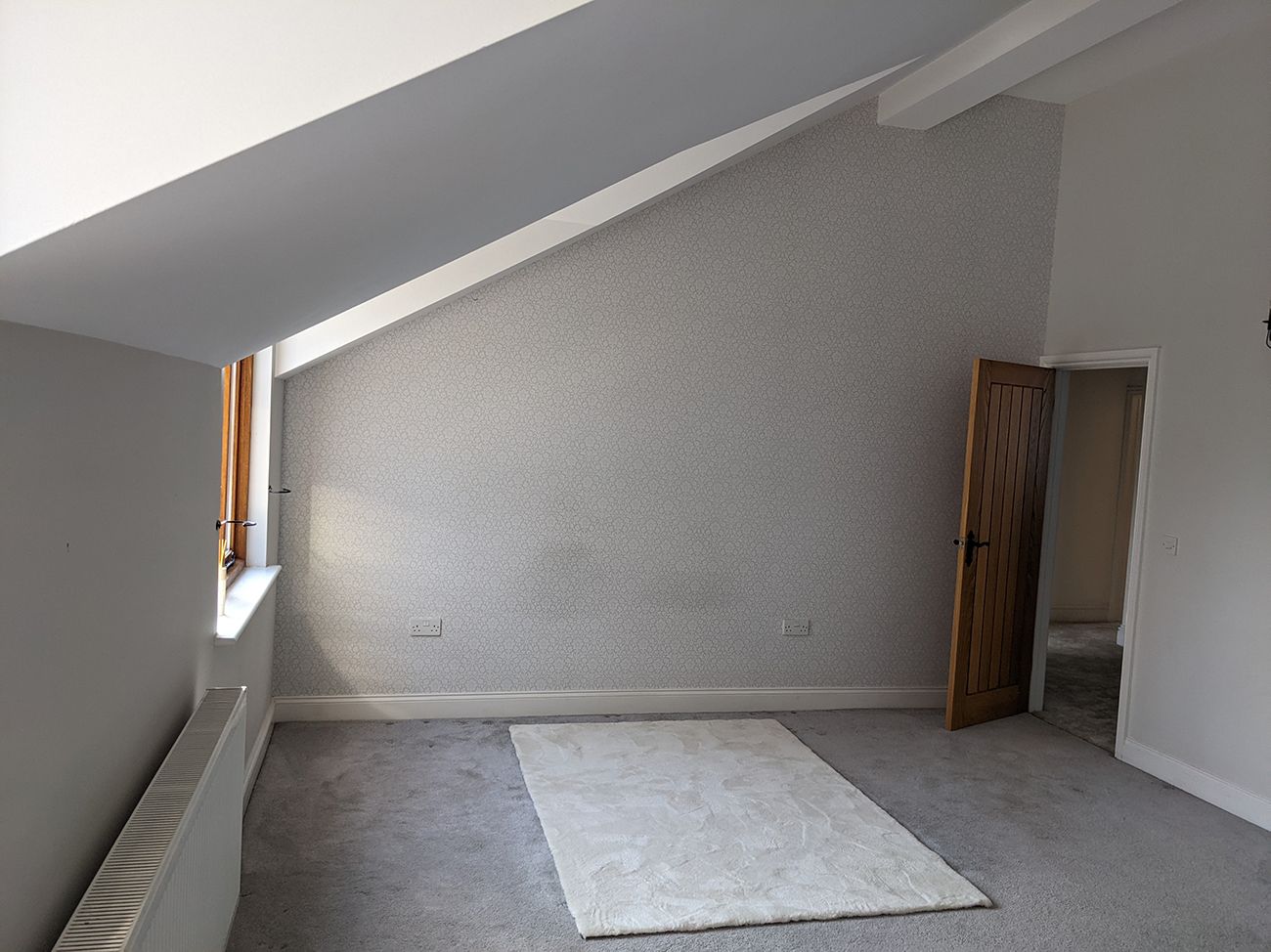 A before photo of the bedroom which had dull grey walls and a grey carpet.
